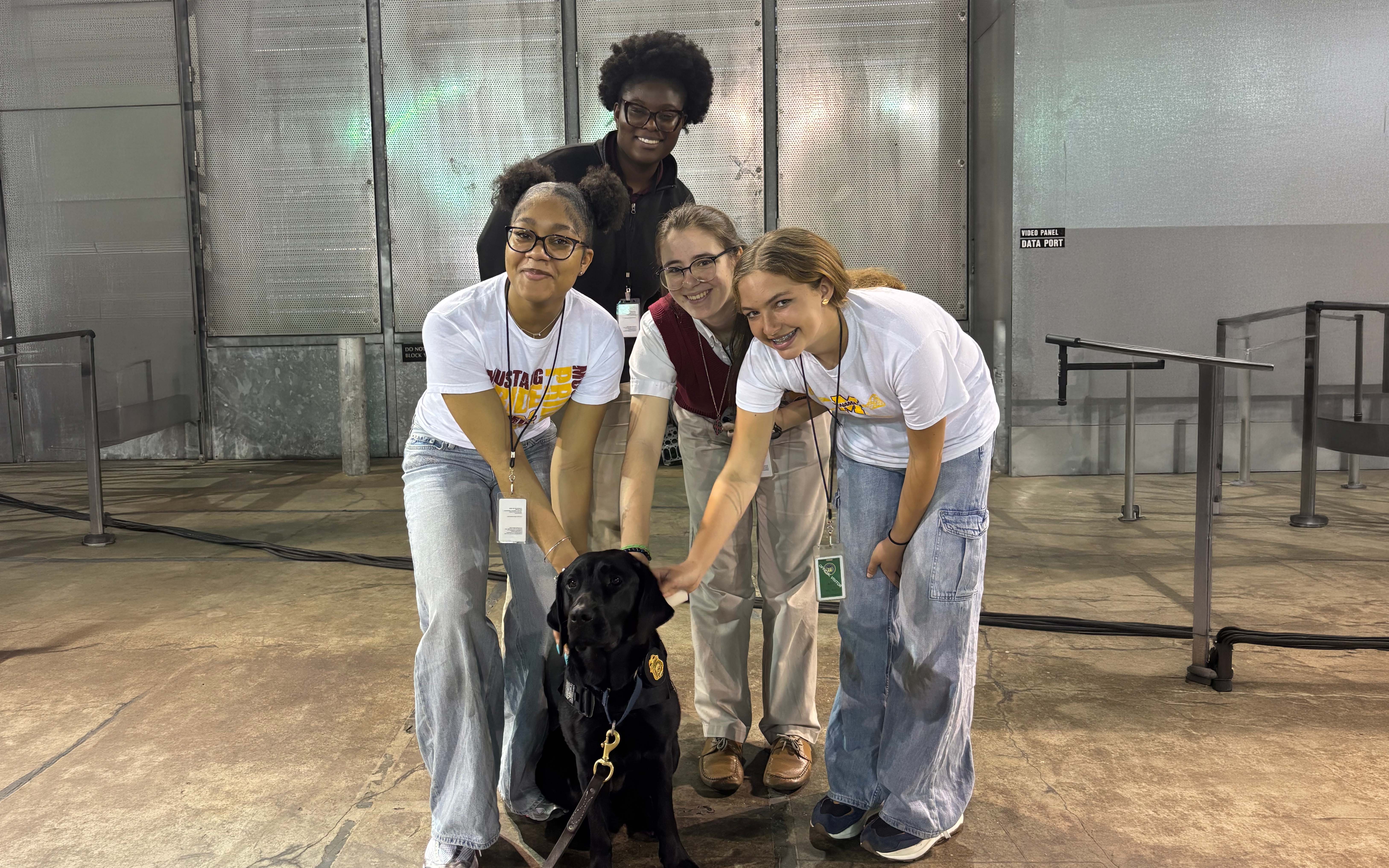 Three high school students extending their arms to pet a K-9 labrador retriever.